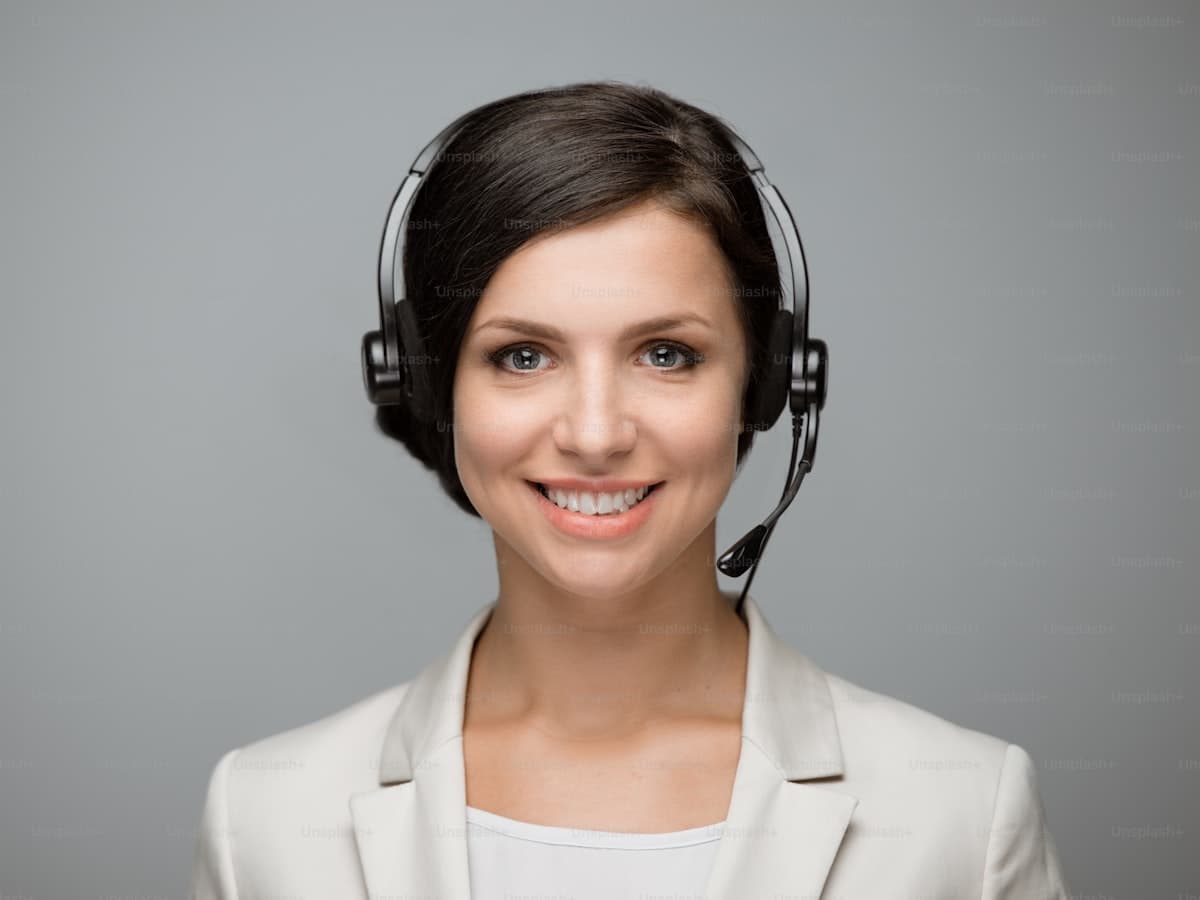 Smiling woman with headphones looking at the camera at a call centre on a grey background